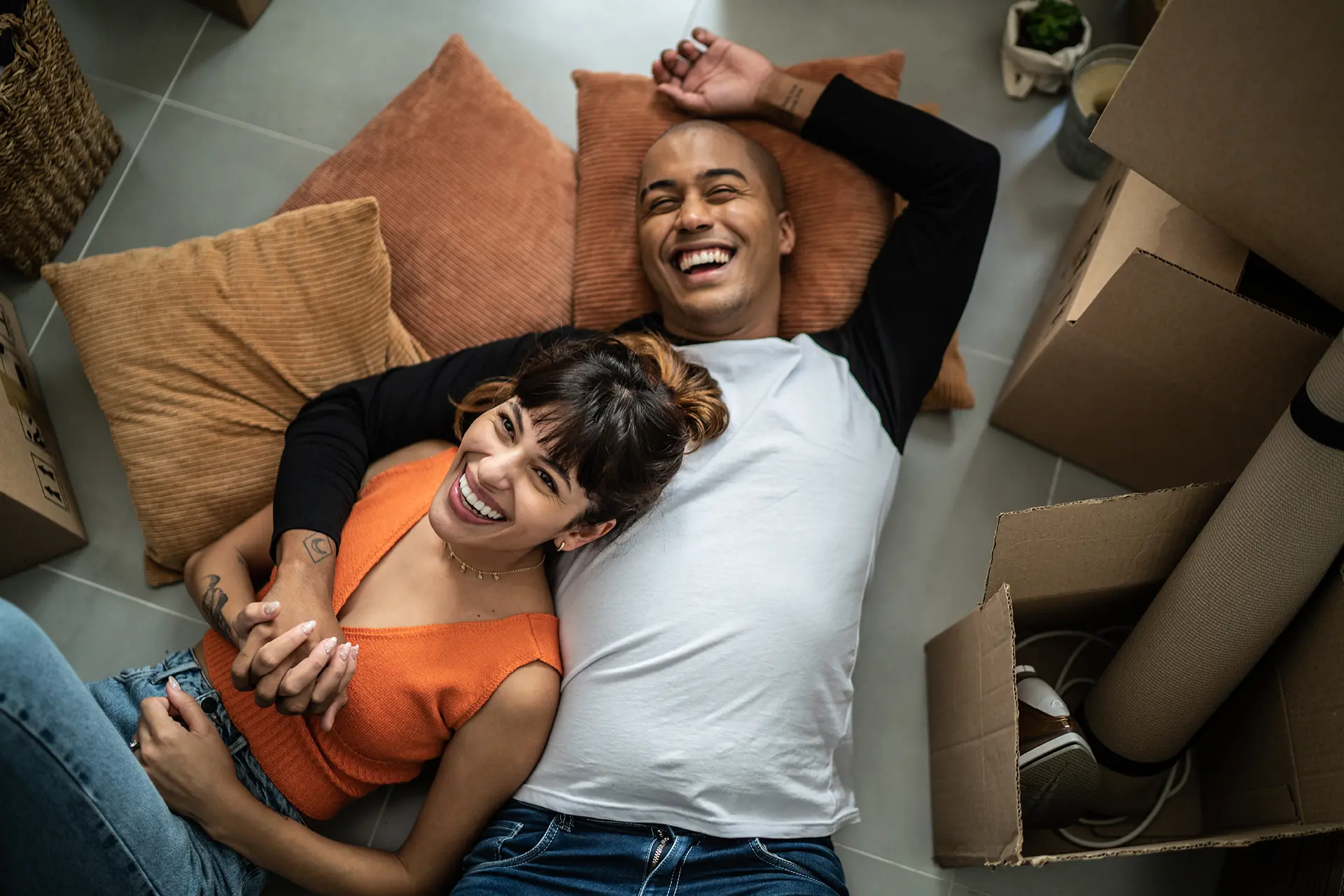 Young couple laughing and lying on pillows to take a break from moving in.