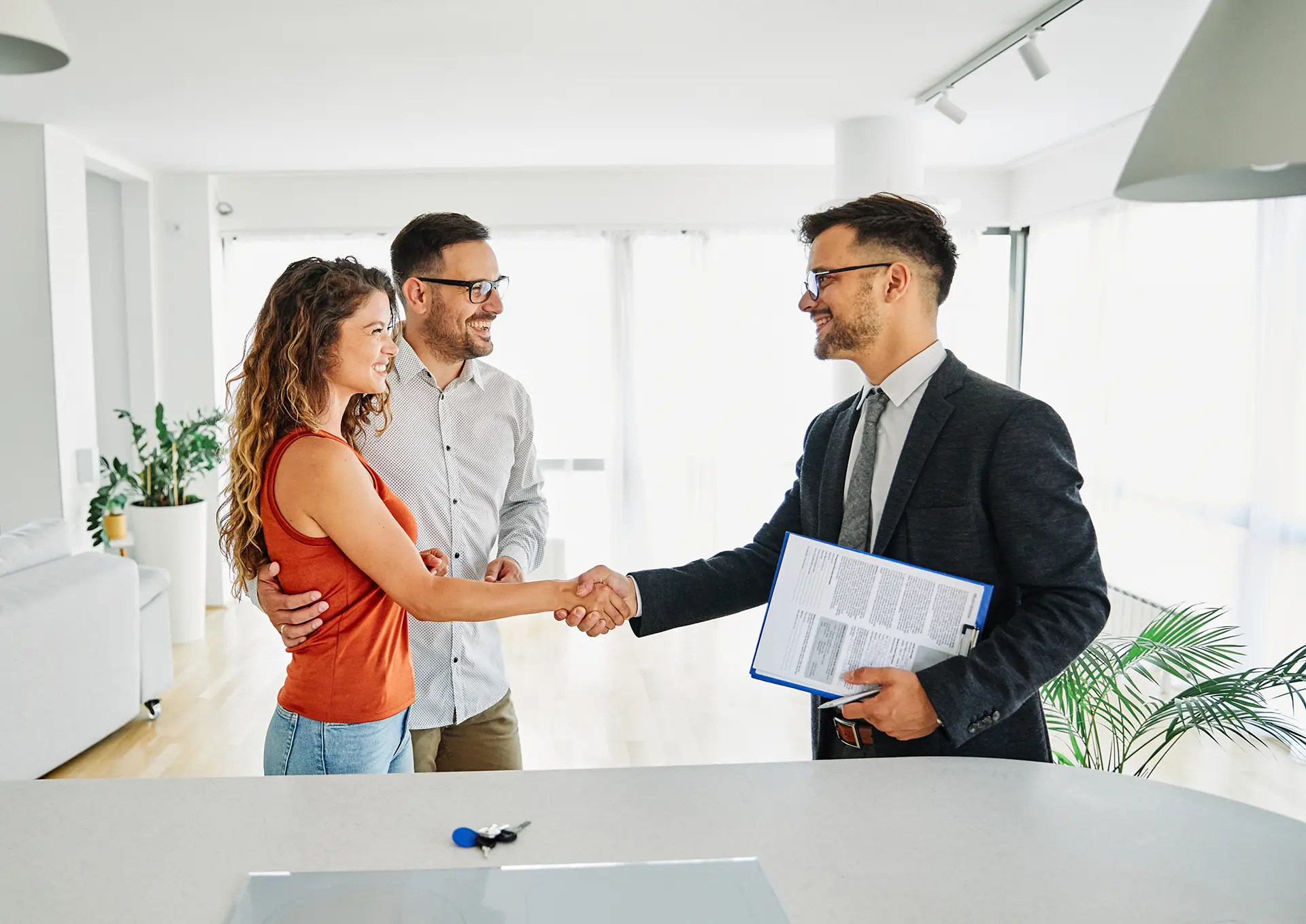 Young couple shaking hands with a real estate agent in a bright open living room.