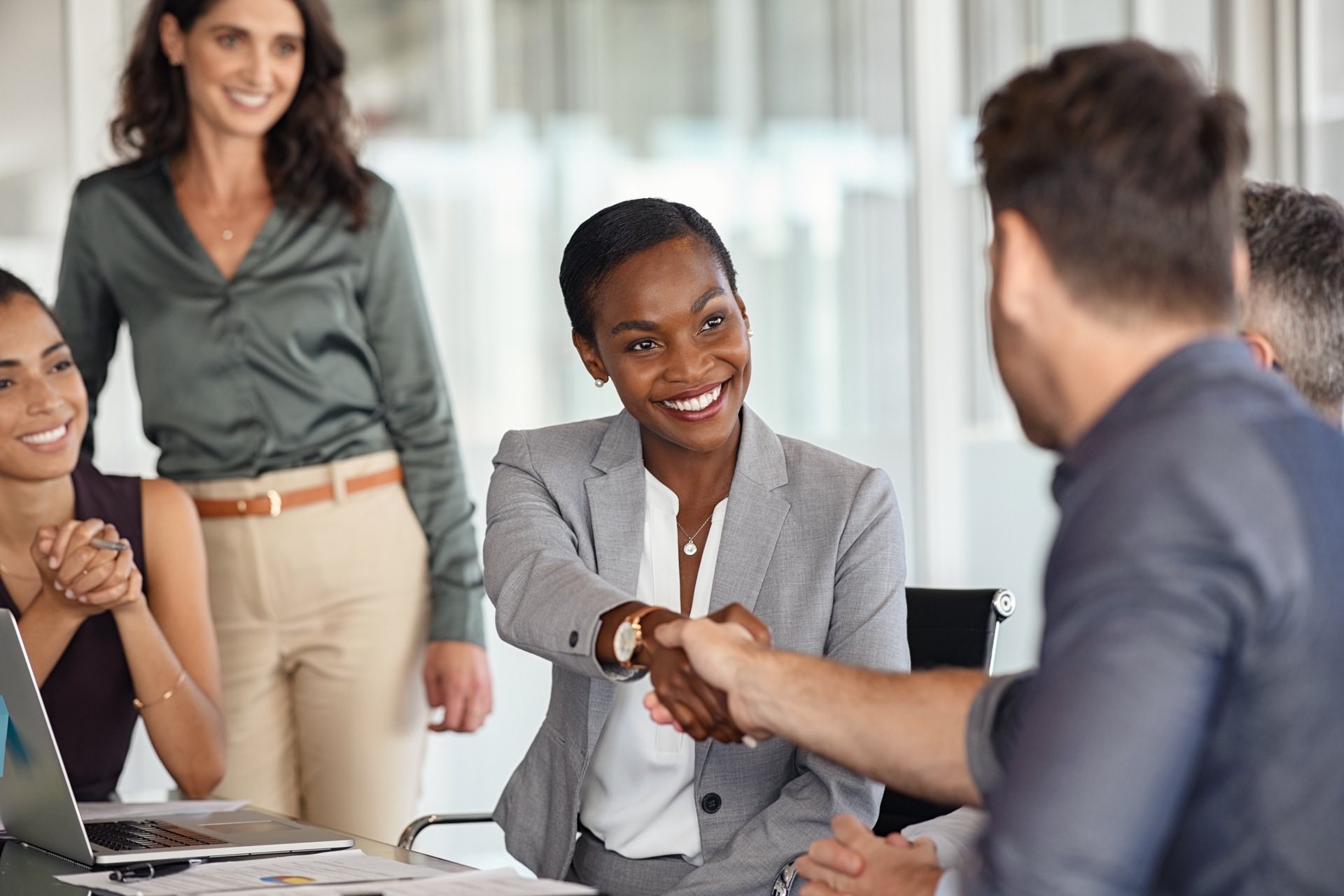 Man and woman shaking hands across a conference table while working out the details of a project.