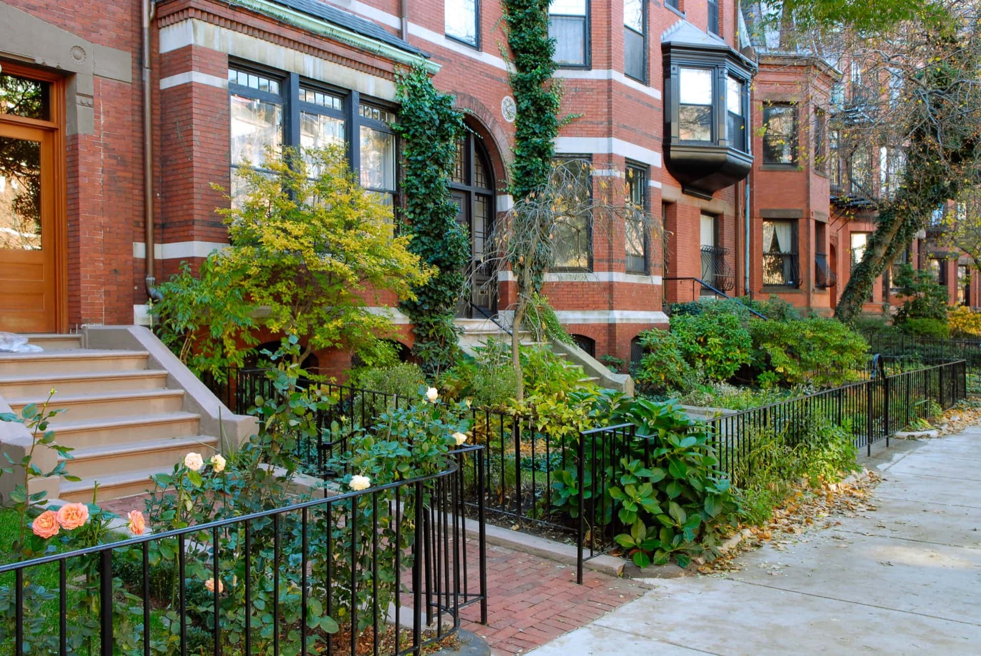 Red brick walk-up townhomes in a row with short black iron fencing.