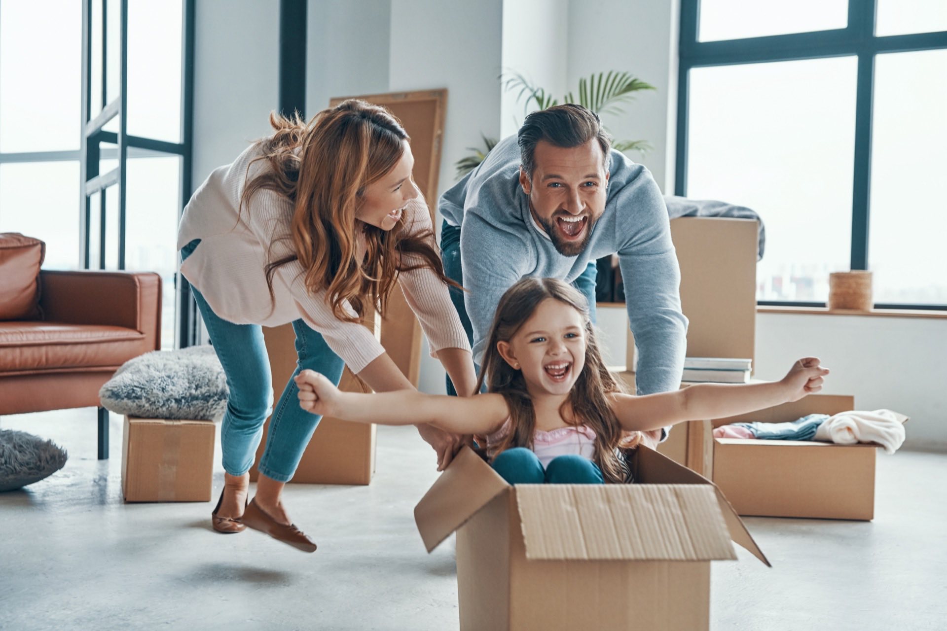 Cheerful family taking a break from unpacking to push their child across the floor in a box.